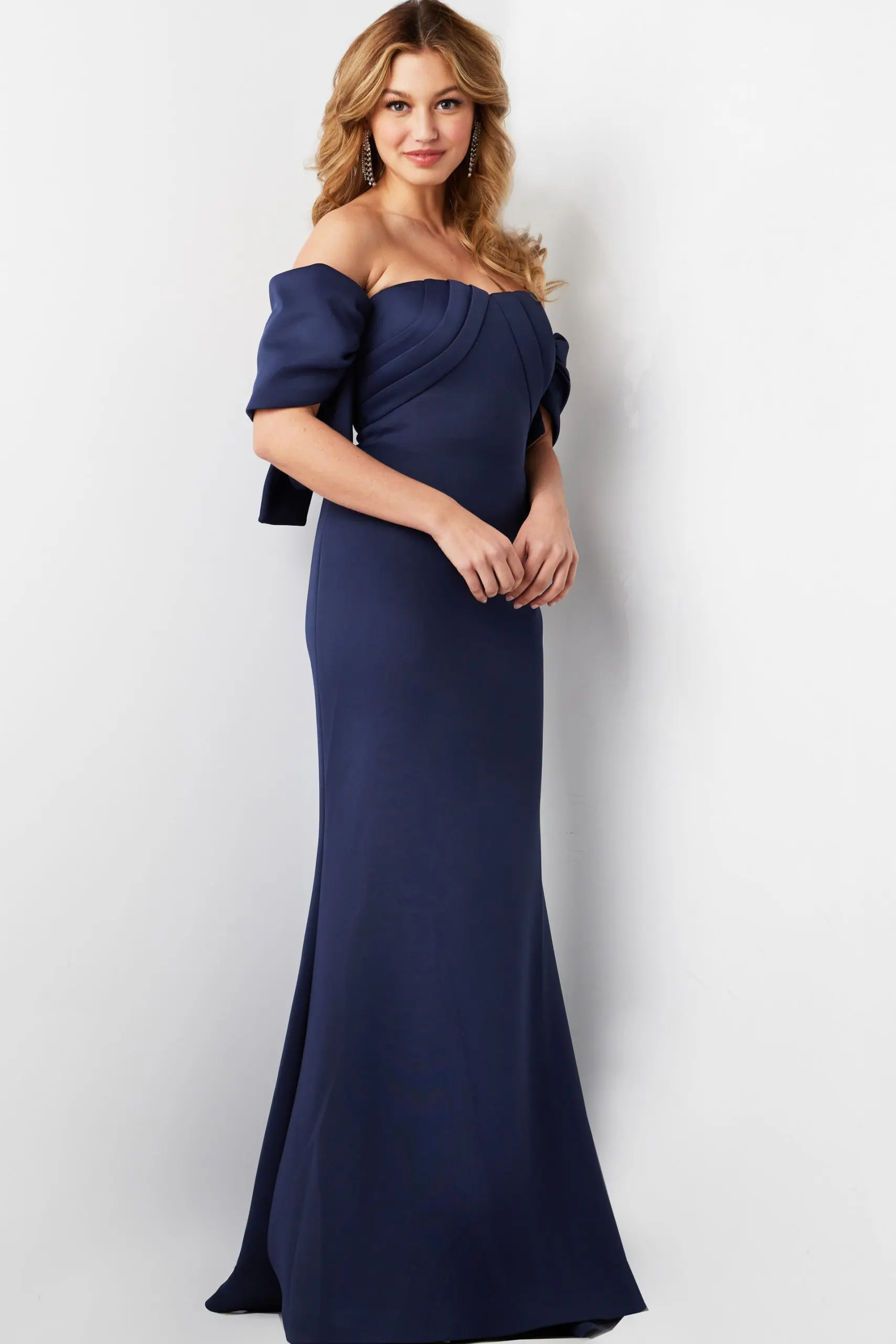 Model wearing Jovani 09064 navy dress with off-the-shoulder design and pleated bodice.