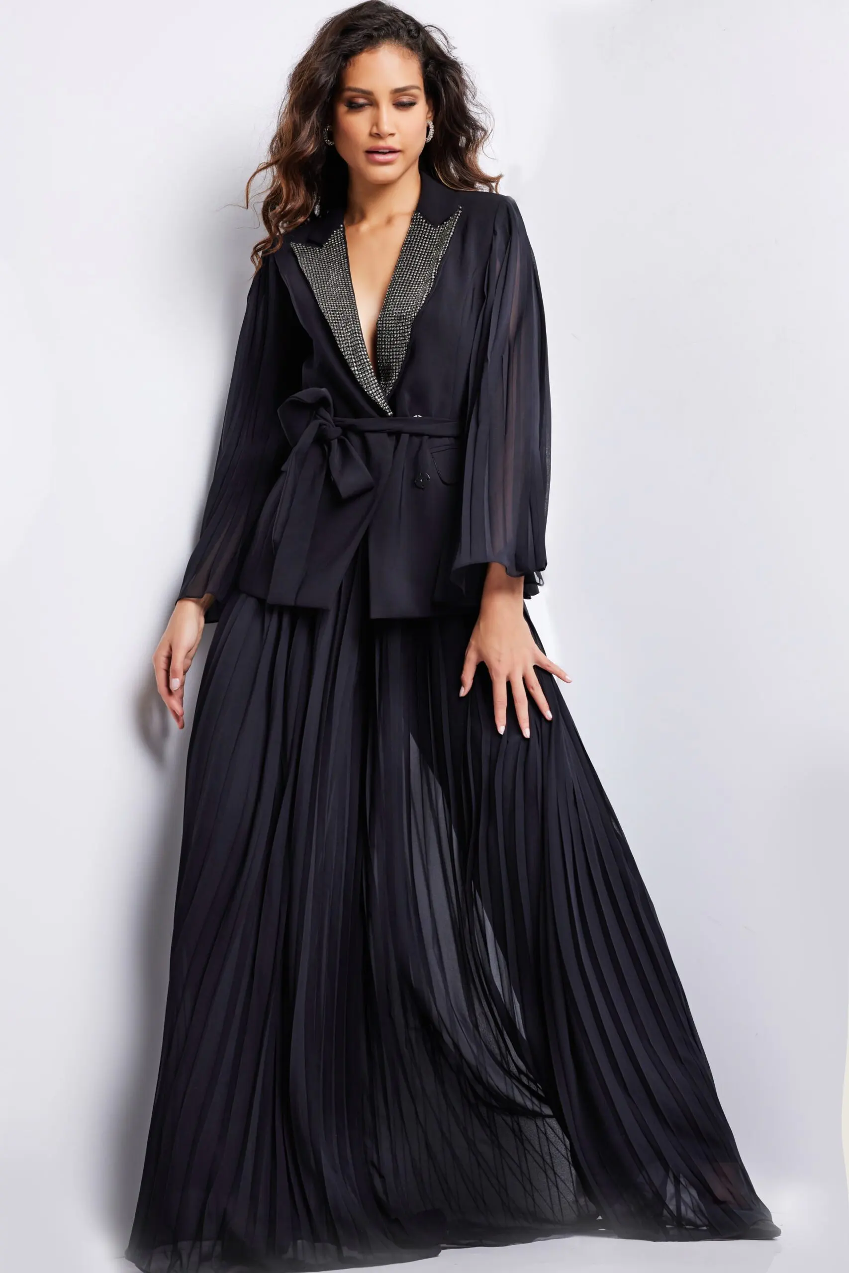 Model wearing Jovani 26024 black gown with beaded lapel and pleated skirt, front view.