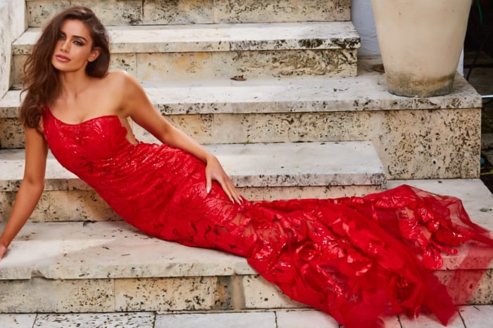 Model wearing Jovani 02895 in red, laying with emphasis on silhouette and beaded detail.