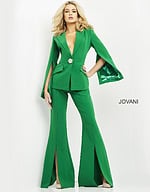 Model wearing Jovani 06922 emerald green jumpsuit with cape sleeves and brooch detail, front view.