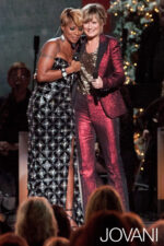 Model wearing Jovani 79121 black gown laughing alongside a person in red.