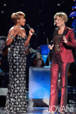 Model wearing Jovani 79121 black gown with another person in a red suit.