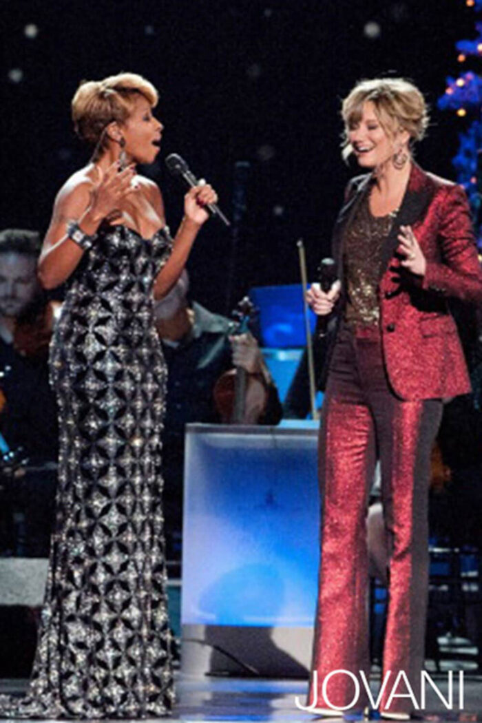 Model wearing Jovani 79121 black gown with another person in a red suit.