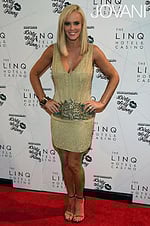 Model wearing Jovani 20711 gold mini dress with V-neckline on the red carpet.