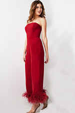 Model wearing Jovani 22590 red strapless jumpsuit with feathered hems, side view.