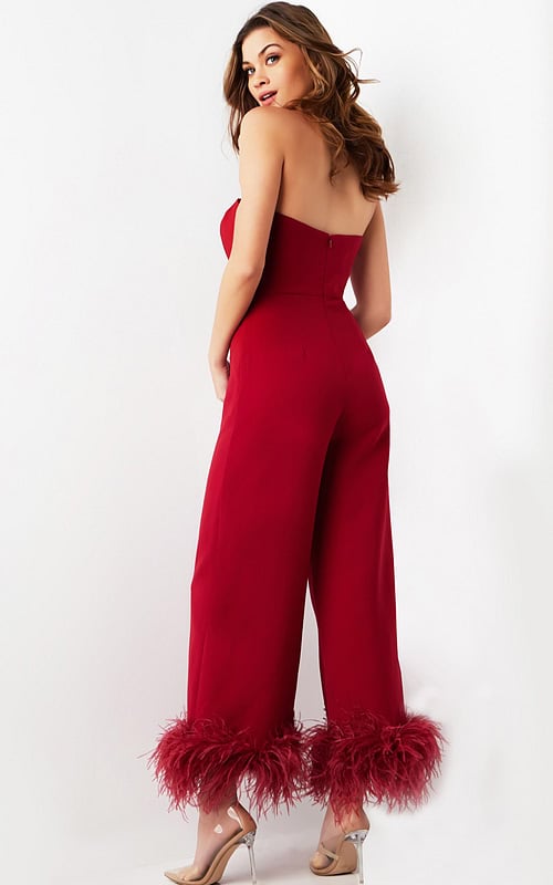 Model wearing Jovani 22590 red strapless jumpsuit with feathered hems, back view.
