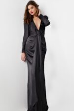 Model wearing Jovani 23180 elegant black gown with deep V-neckline and knot detail, angled front view.