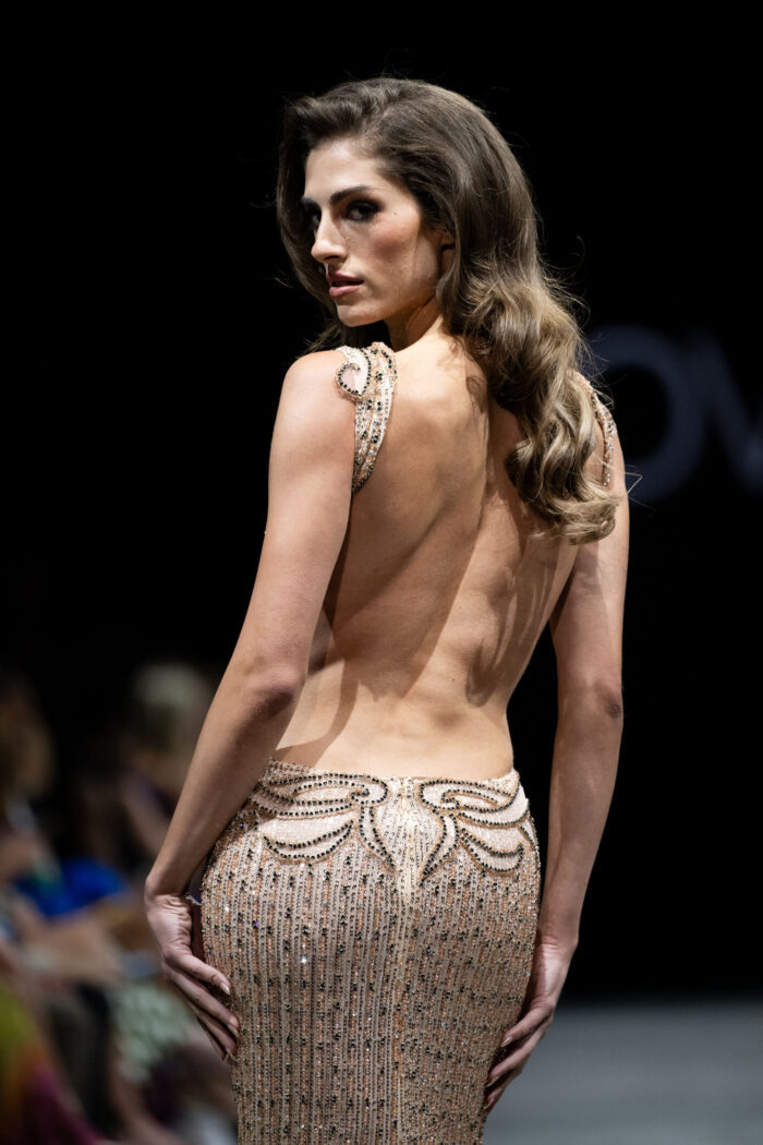 Model wearing Jovani 23896 blush dress with backless design, showcasing detailed embellishments, back view.