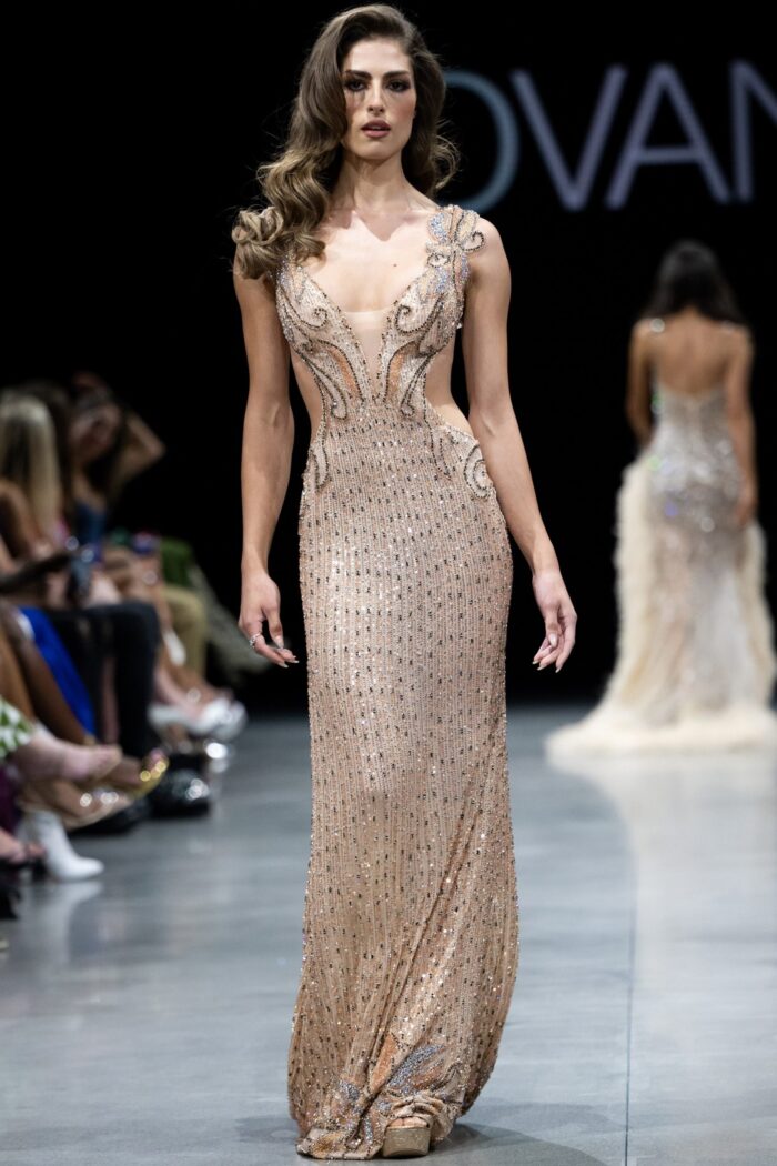 Model wearing Jovani 23896 blush dress with elaborate beading and deep V-neckline, front view.