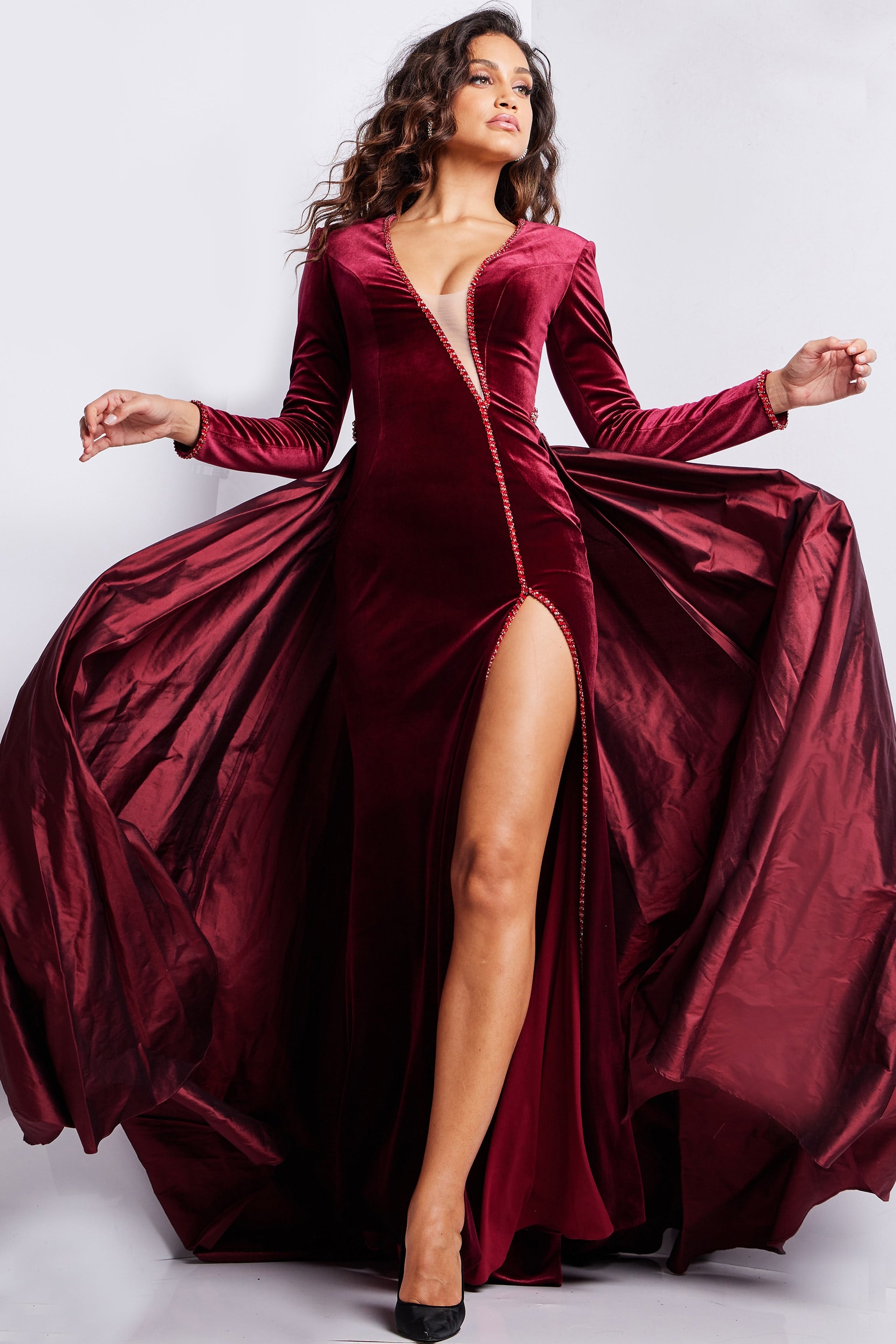23943_BURGUNDY.jpg Model wearing Jovani 23943 burgundy gown with deep V-neckline and high slit, front view.