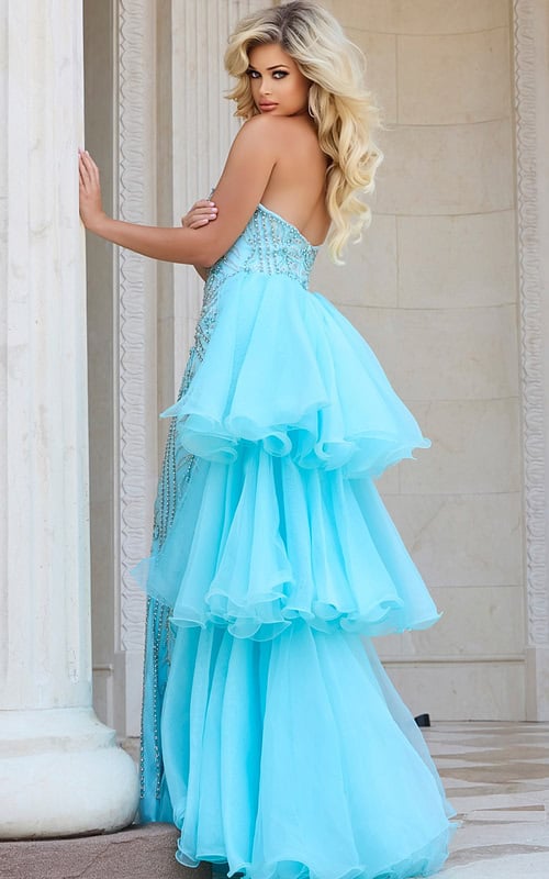 Model wearing Jovani 24565 blue gown with cascading ruffles, back view.