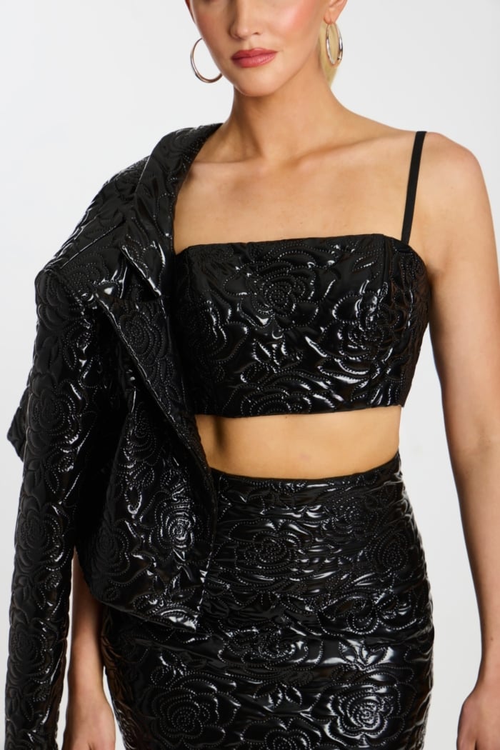 Close-up of crop top and skirt with detailed embossed floral design in black patent fabric.