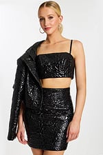 Model wearing cropped black embossed jacket over shoulder, showing strap top and high-waisted skirt.