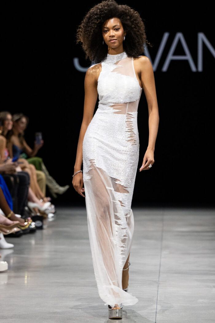 Model wearing Jovani 25974 elegant white dress with sheer details and high slit.