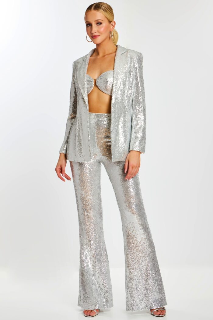 Model wearing silver sequin pantsuit with flared trousers, bralette top, and open blazer.