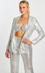 Model posing in silver sequin bralette, blazer, and matching high-waisted pants with hand on hip.