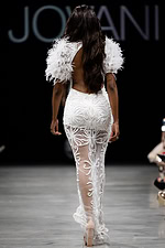 Model wearing Jovani 26057 white dress with an open back and feathered sleeves, back view.