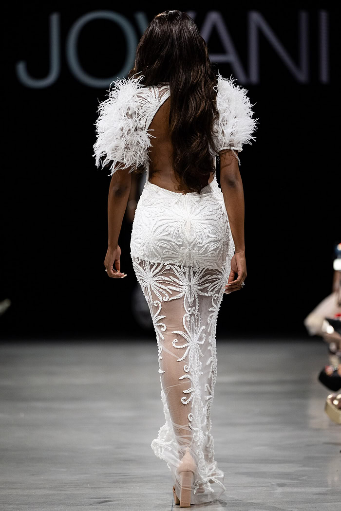 Model wearing Jovani 26057 white dress with an open back and feathered sleeves, back view.