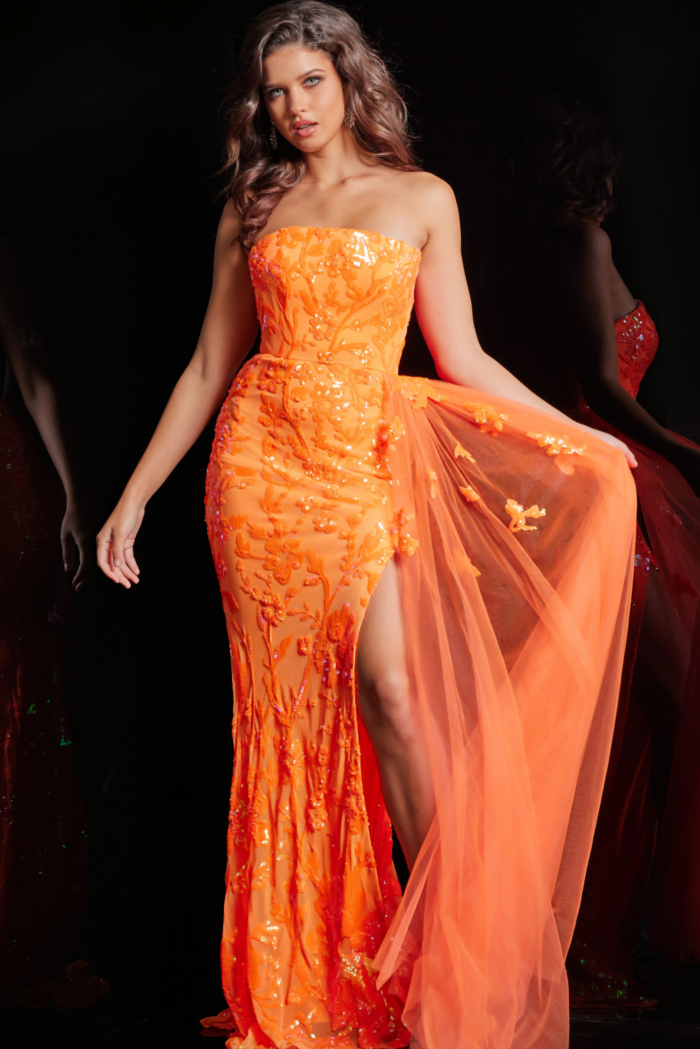 Model wearing Jovani 26134 orange dress featuring floral embellishments.