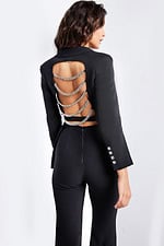 Model wearing Jovani 26144 black pantsuit with open back and chain detailing.