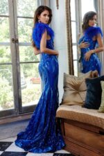 Model wearing Jovani 32596 royal blue gown with feather detail at shoulder, back view.