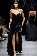 Runway model in Jovani 34392 black gown with embellished straps and ruffled slit.