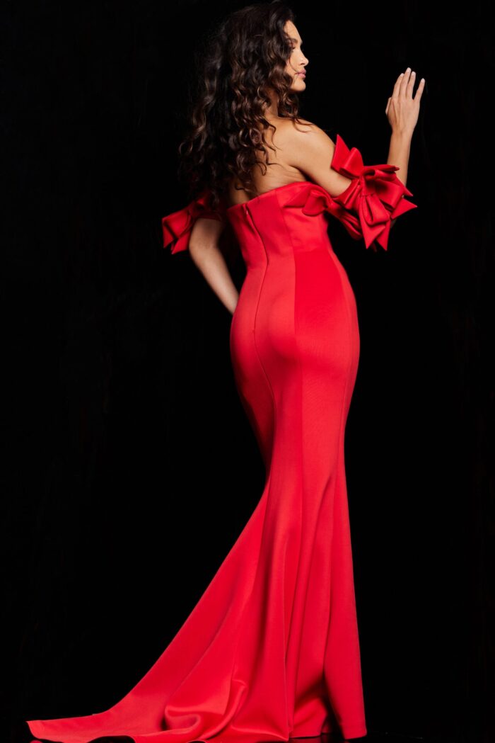 Model from behind in Jovani 36997 red mermaid gown with flared skirt and dramatic sleeve bows.