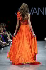 Model showcasing back of Jovani 37254 orange gown with floral one-shoulder detail.