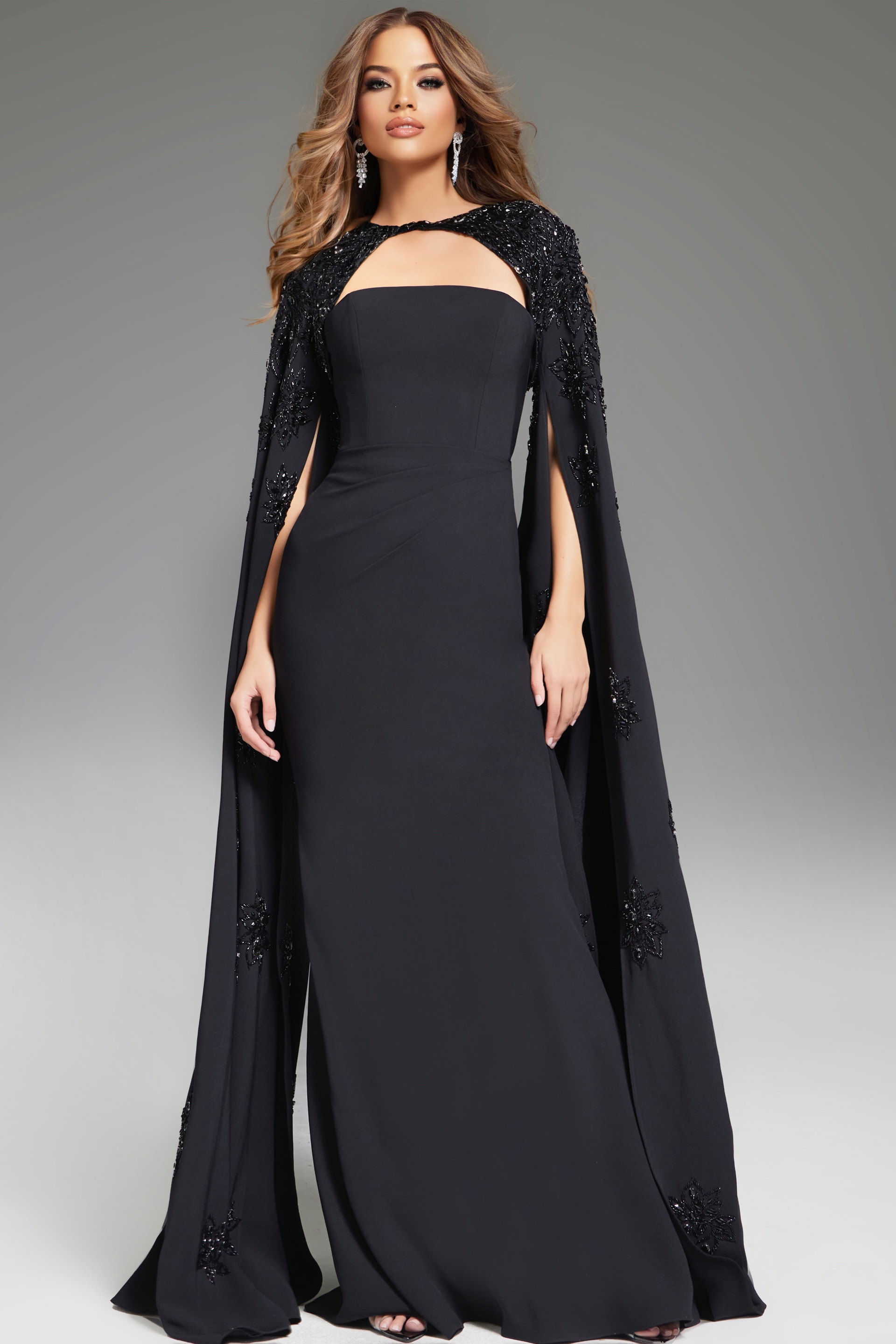 39957 model wearing Jovani 39957 floor-length black gown with strapless neckline and embellished cape