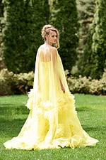 Model wearing Jovani 40092 yellow gown with flowing tulle and floral details, angled back view