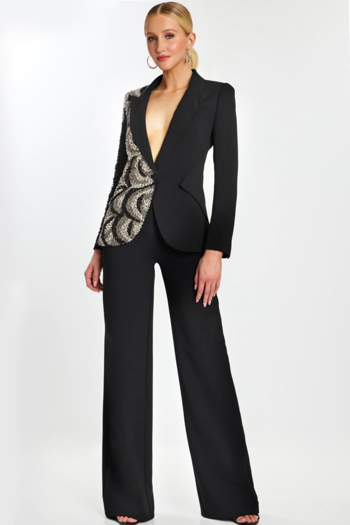 Model wearing black pantsuit with asymmetric sequin detailing and plunging neckline.