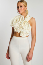 Angled view showing structured floral appliqué on one-shoulder crop top paired with sleek pants