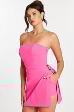 Front angle of a woman holding the overlay skirt of a hot pink romper with visible pocket.