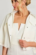 Model looking down wearing white structured jumpsuit and cape jacket