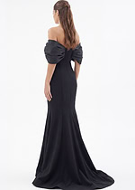 Black off-the-shoulder mermaid evening gown with dramatic puff sleeves and flowing train, model holding skirt.