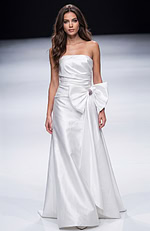 Strapless floor length gown with a smooth fitted bodice, soft draping, and an oversized bow detail at the waist creating a clean, elegant silhouette