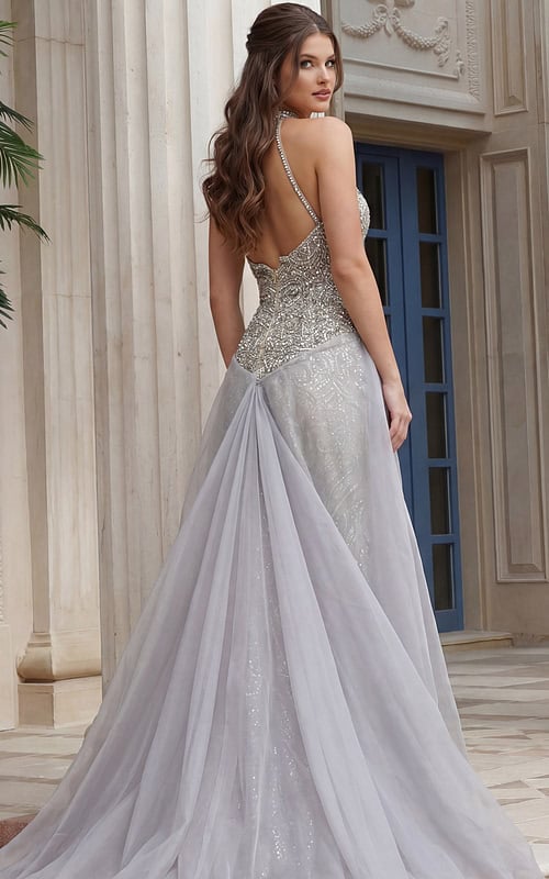 Back view of beaded halter style dress with open back, fitted waist, and flowing sheer overskir