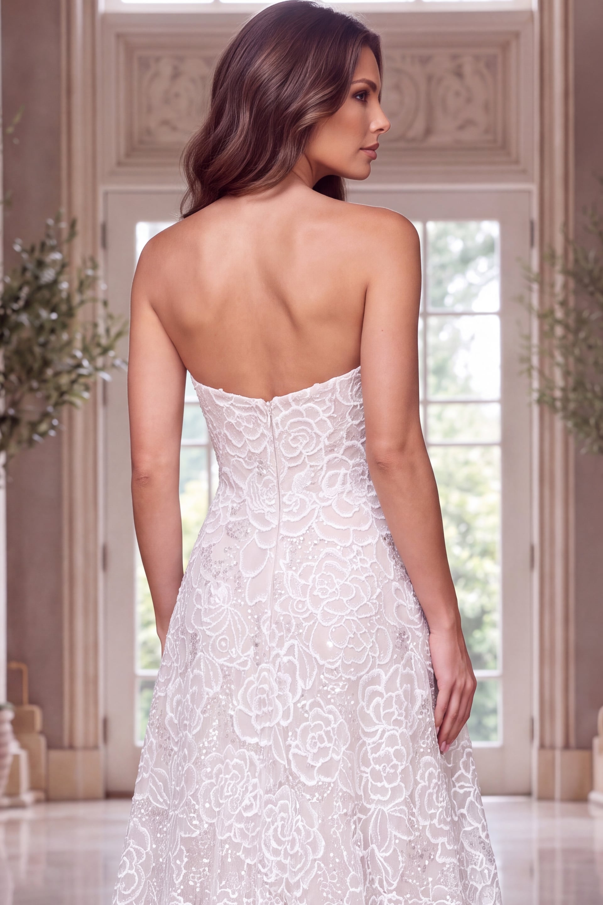 Rear crop framing the bare shoulders, back zip and floral lace skirt of a strapless gown