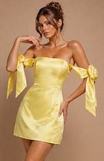 Radiant yellow satin party dress with an off-the-shoulder silhouette and long, flowing bow accents.