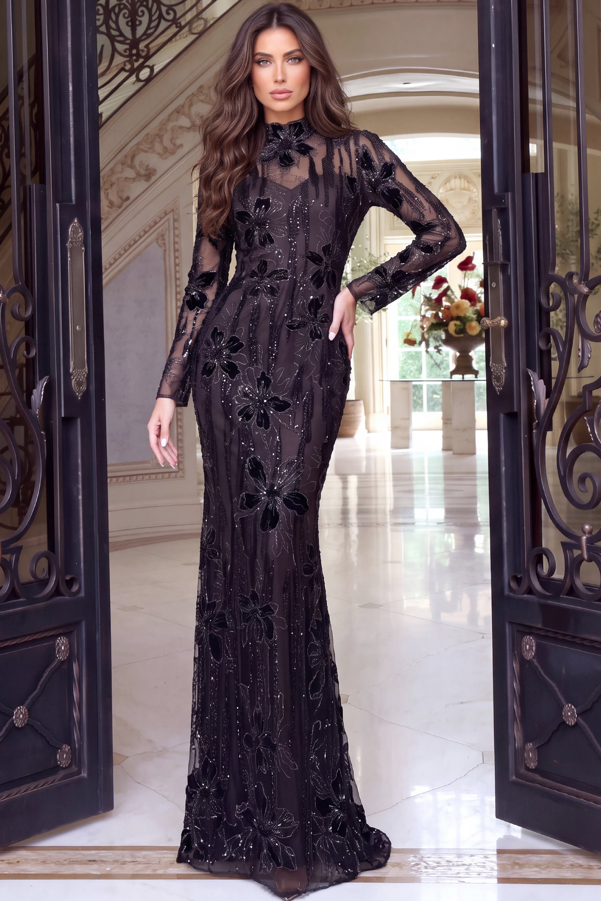 Floor-length black gown covered in velvet flowers, sheer sleeves and mock neckline