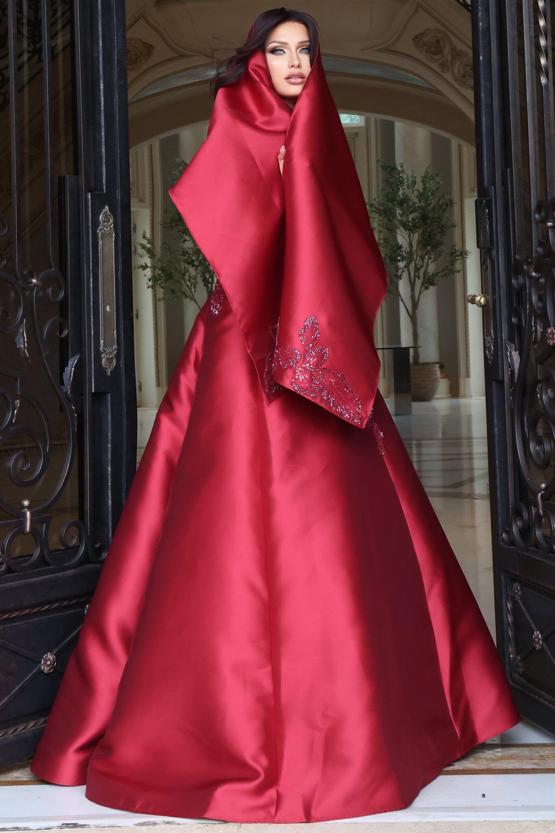 Deep red satin gown with dramatic draped hooded shawl and beaded sleeve accent