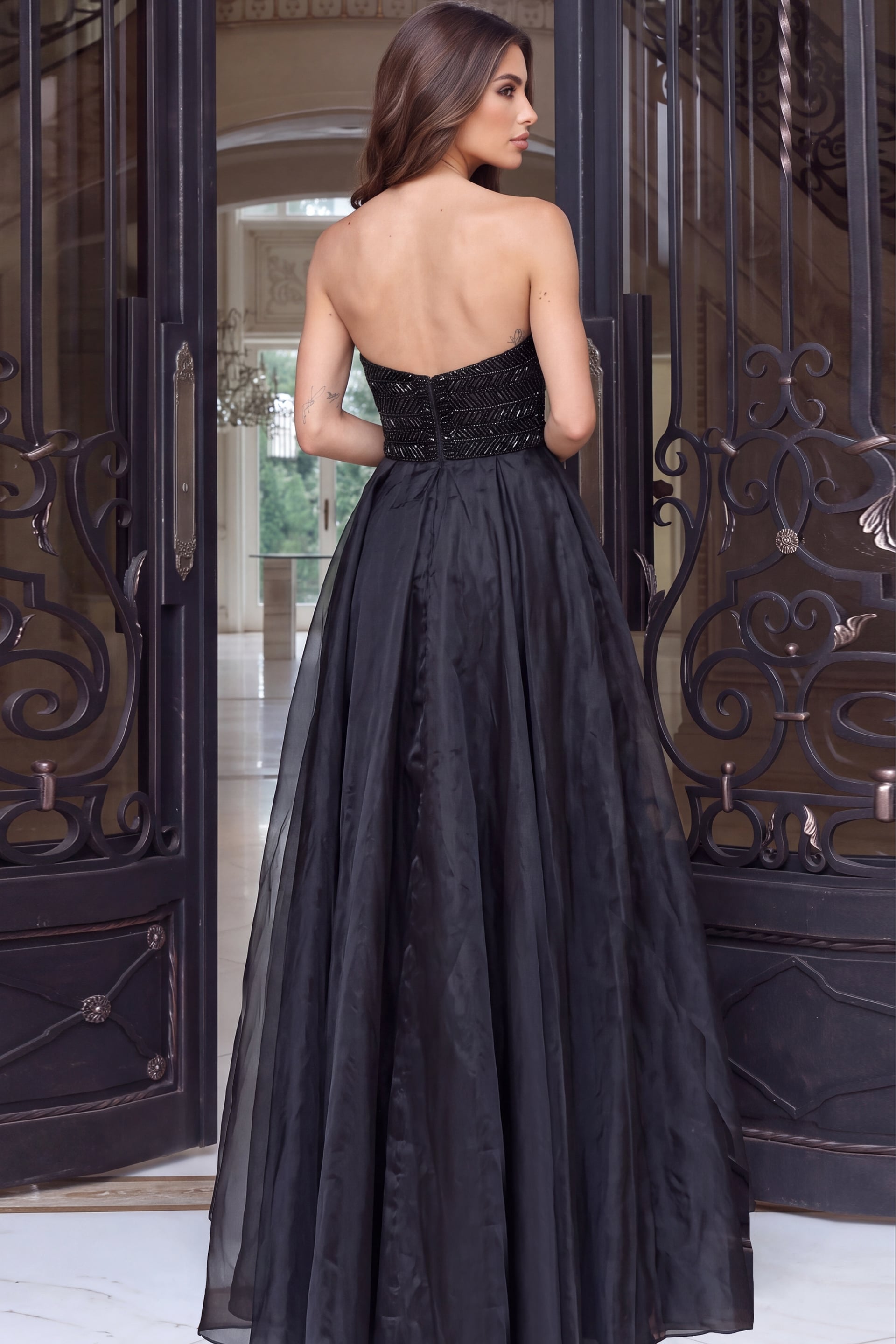 Beaded strapless gown viewed from the rear, billowing organza overskirt and bare open back