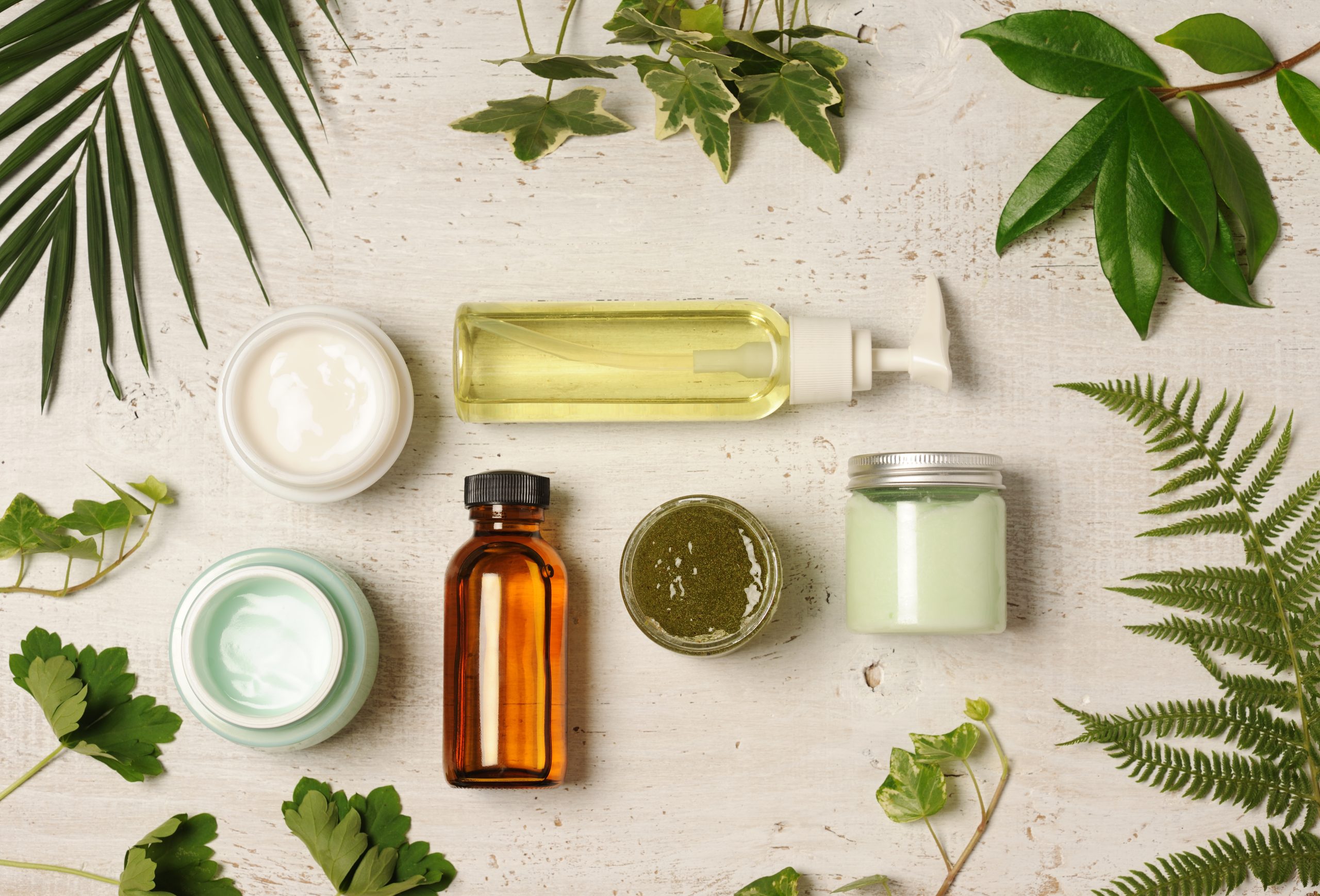 Various beauty product containers surrounded by various leaves.