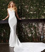 Model wearing Jovani JB03910 white dress with mermaid silhouette, leaning against a railing.