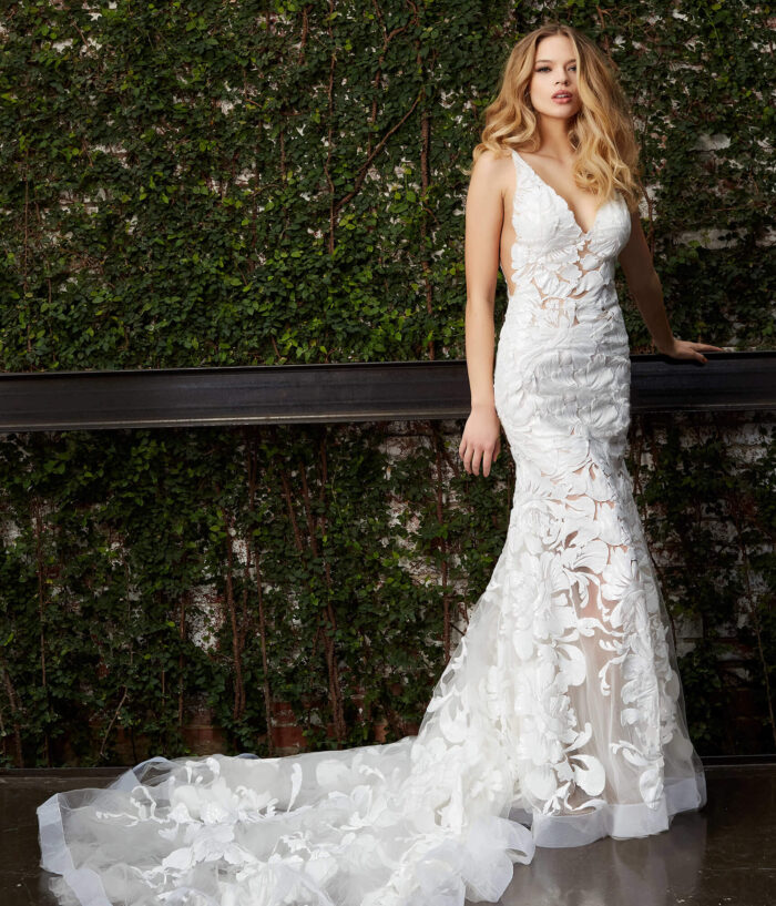 Model in Jovani JB04192 white gown with floral design standing next to greenery