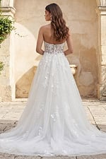 Back view of a strapless lace gown with button closure and flowing tulle skirt with floral appliqués.