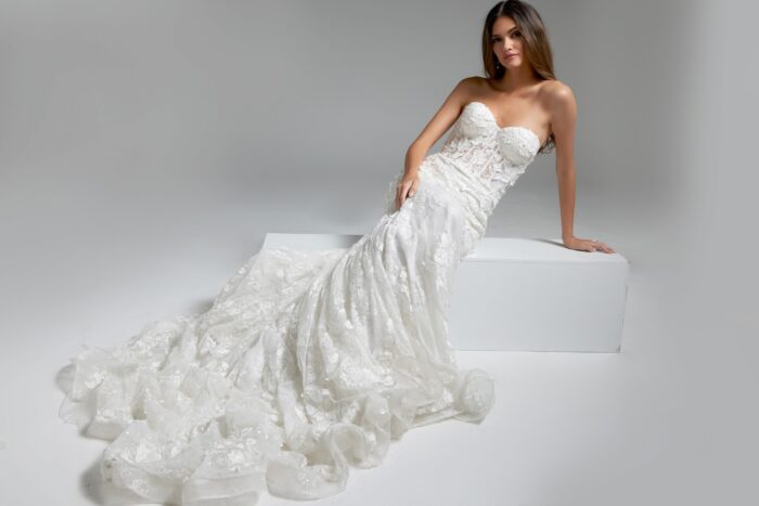 Model in Jovani JB07583 white gown reclining, highlighting mermaid silhouette and floral accents.