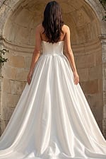 Back view of a strapless satin bridal gown with pleated ball skirt and chapel train set against stone arches