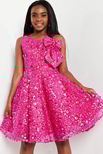 model wearing K23682 fuchsia dress with floral embellishments and shoulder bow, holding skirt up
