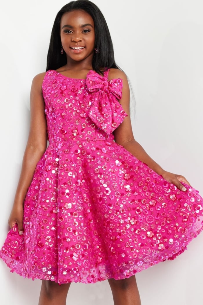 model wearing K23682 fuchsia dress with floral embellishments and shoulder bow, holding skirt up